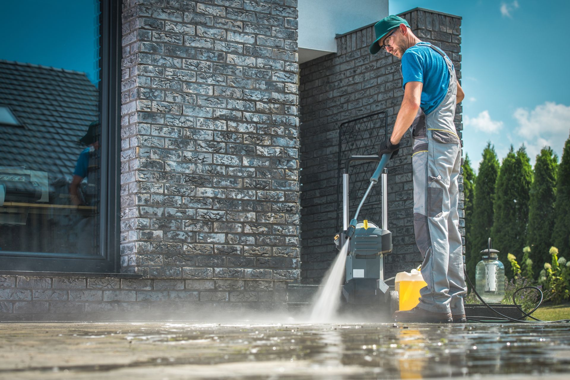 A man is using a high pressure washer to clean the sidewalk in front of a brick building.