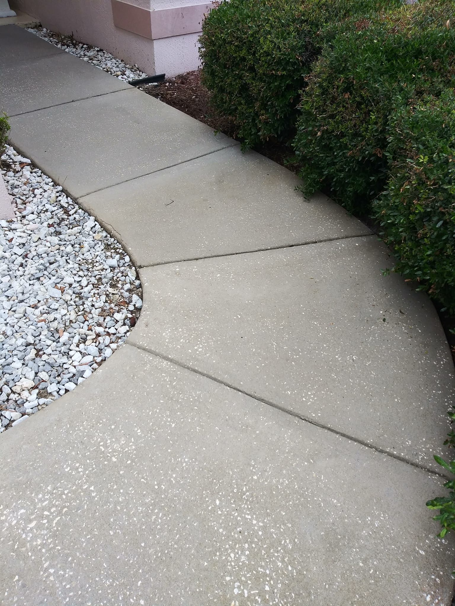 A sidewalk with a bush and gravel on the side of it.