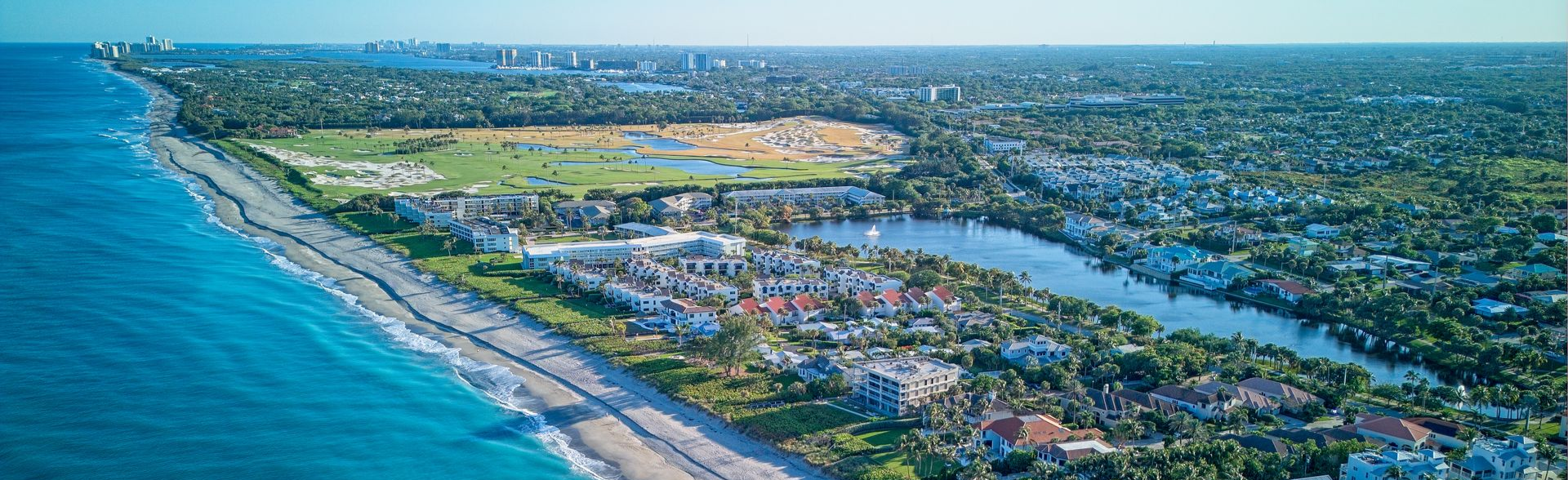 Aerial view of a coastal resort with beaches, ocean, and a large green park inland