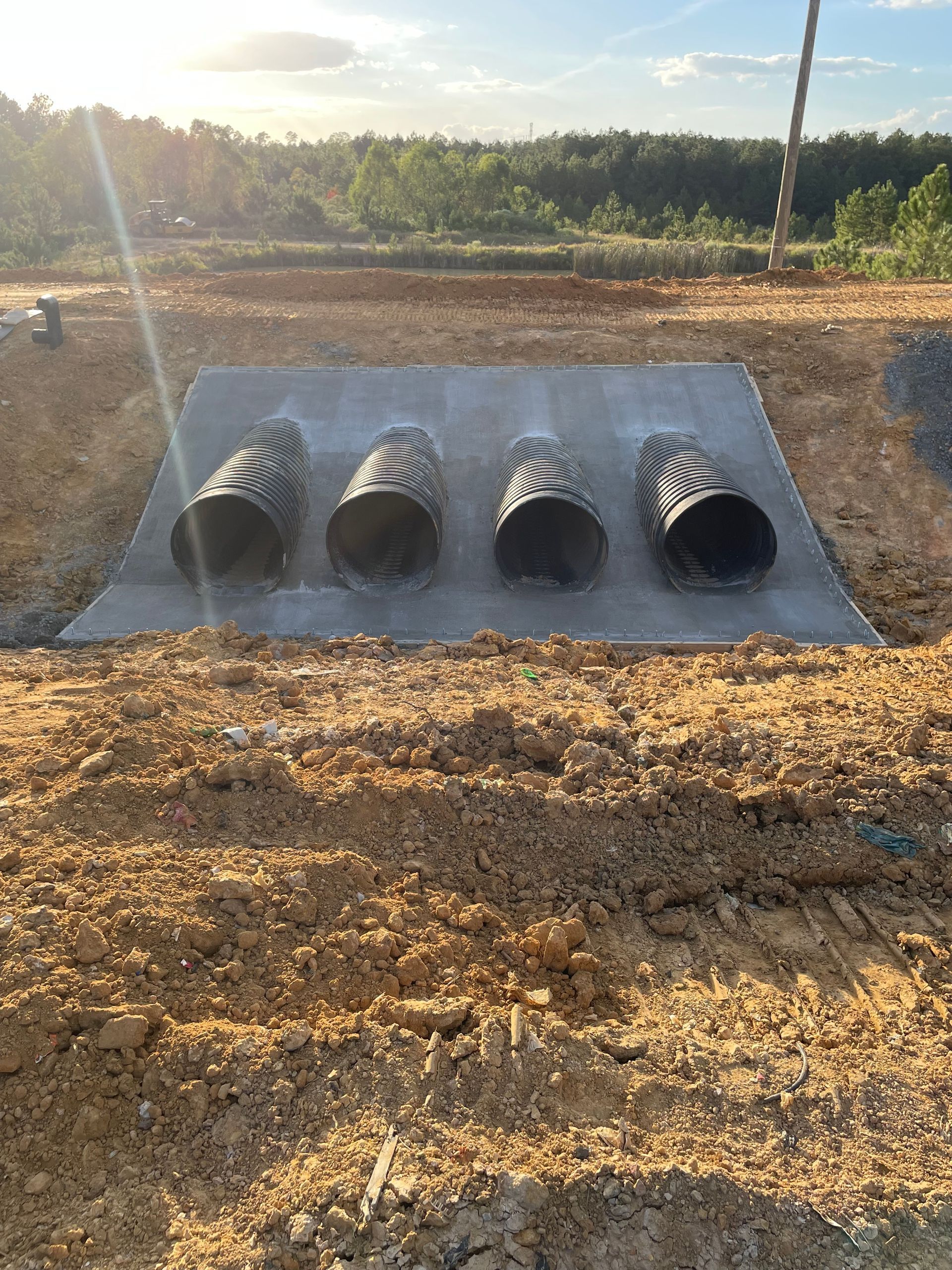 four black pipes are sitting on top of a concrete slab in the dirt .