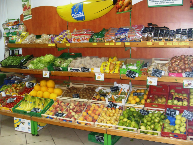 Banco di frutta e verdura ricco di colori, tra cui banane, arance, mele e verdure a foglia verde.