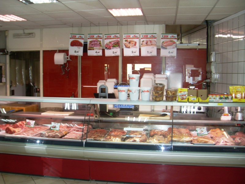 Bancone di macelleria con vetrina espositiva di carni e menù in rosso e bianco sullo sfondo.
