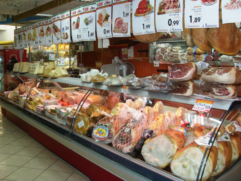 Banco gastronomia con salumi, insaccati, formaggi e cartellini dei prezzi in una bancarella del mercato.