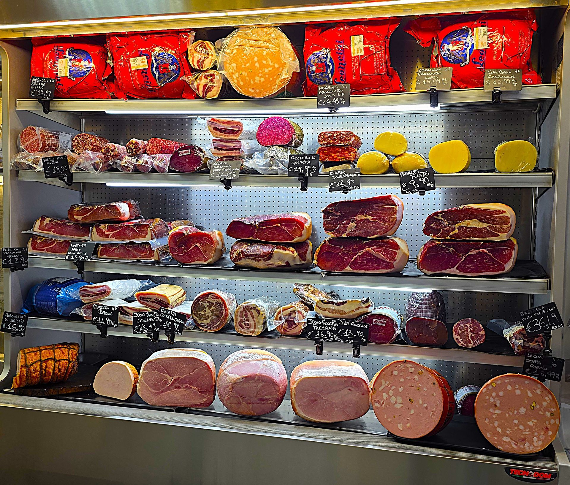 Banco gastronomia con salumi, insaccati, formaggi e cartellini dei prezzi in una bancarella del mercato.