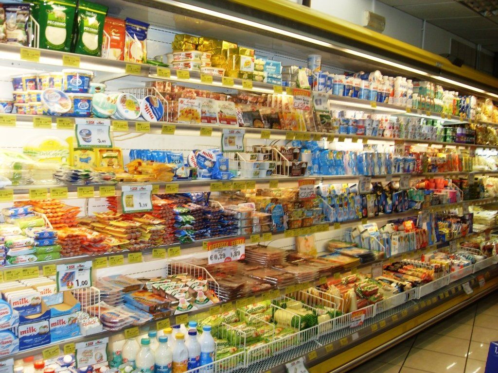 Reparto latticini di un supermercato con scaffali pieni di yogurt, formaggi, bevande e alimenti confezionati.