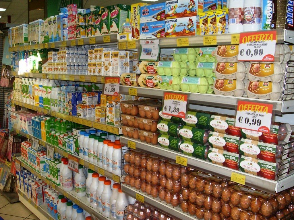 Corridoio di un supermercato con scaffali pieni di prodotti alimentari confezionati, barattoli e cartoni del latte con cartelli di sconti.