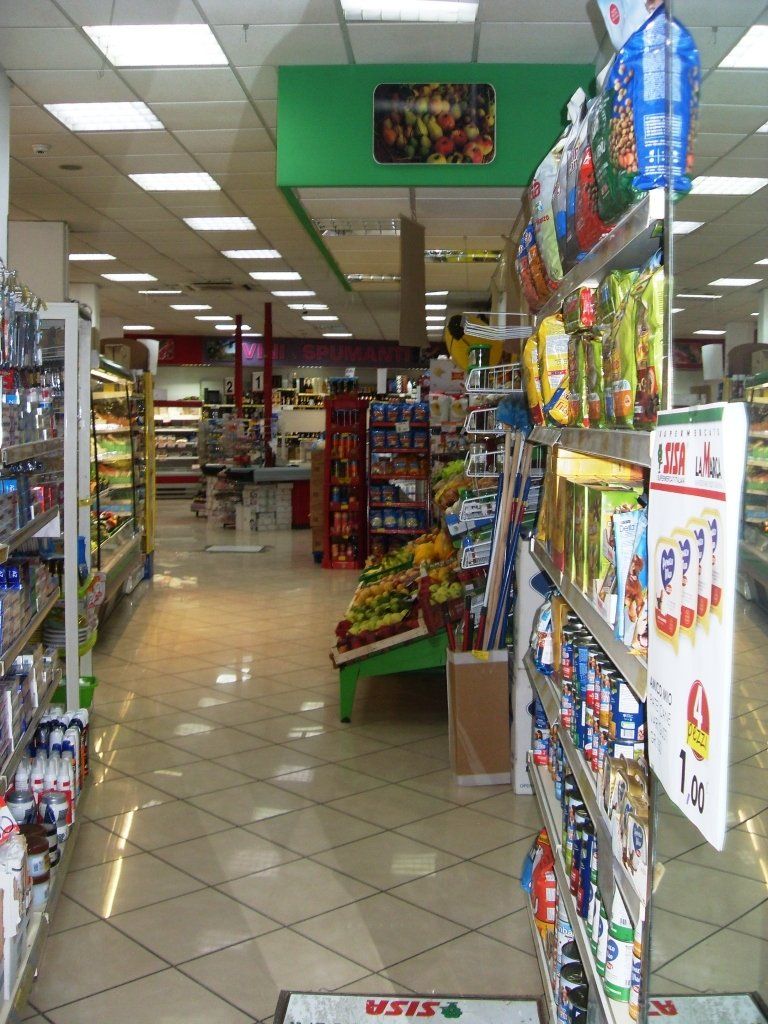 Un corridoio di un supermercato con scaffali pieni di snack e bevande illuminati da luci fluorescenti brillanti.