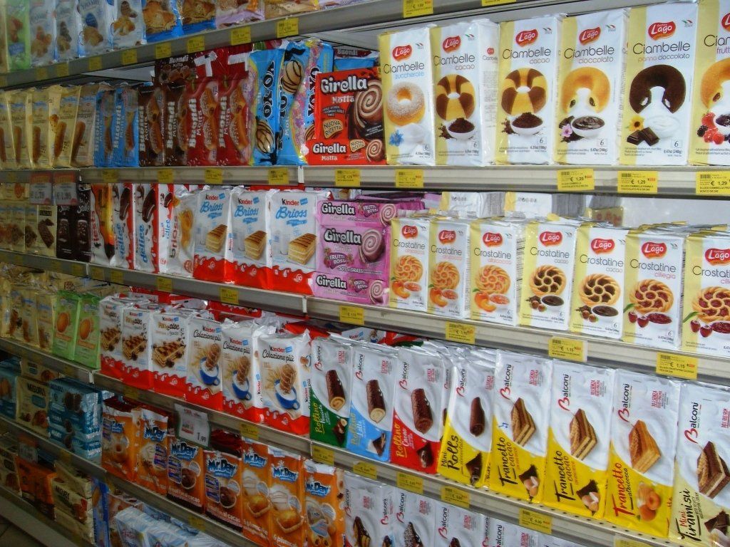 Un corridoio di un supermercato pieno di scatole colorate di cereali e snack su scaffali di metallo.