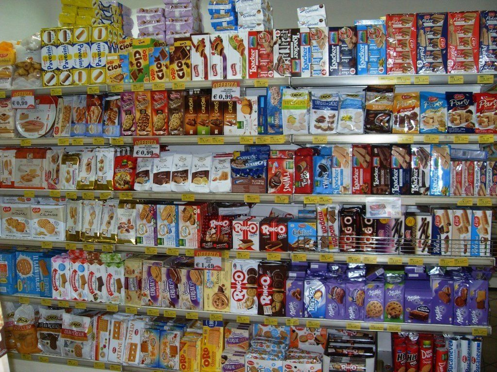 Il reparto snack di un supermercato, con scaffali pieni di patatine, caramelle e snack confezionati in modo colorato.