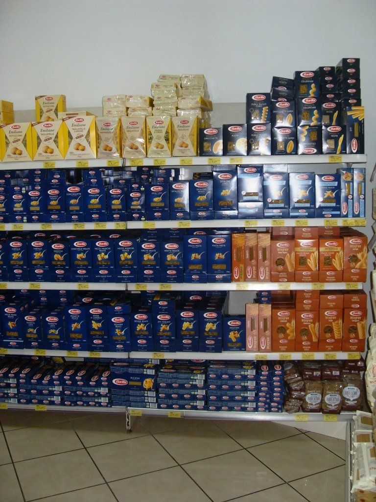 Scaffale del negozio pieno di generi alimentari confezionati in modo colorato e scatole impilate in un corridoio piastrellato.