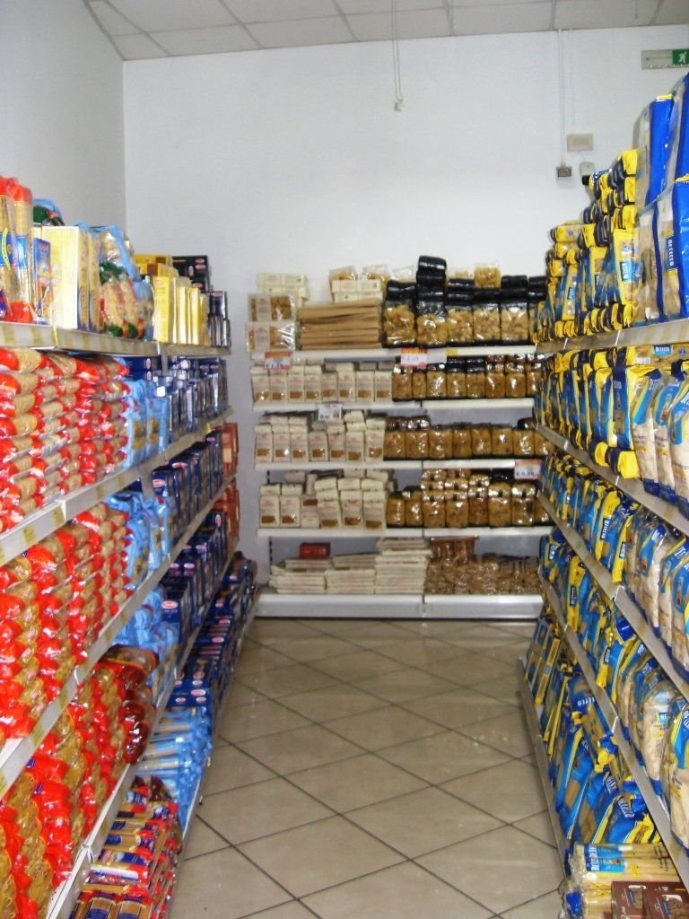 Stretto corridoio del supermercato con scaffali pieni di prodotti confezionati colorati e articoli da dispensa.