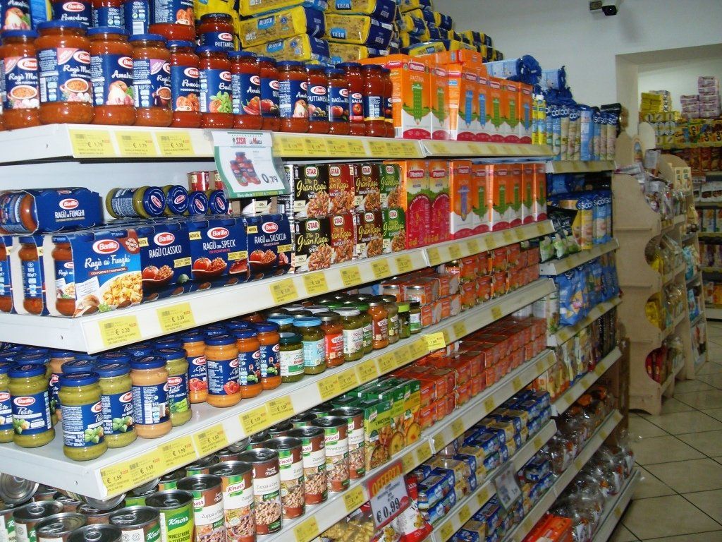 Un corridoio di un supermercato pieno di barattoli colorati, lattine e alimenti confezionati sugli scaffali.