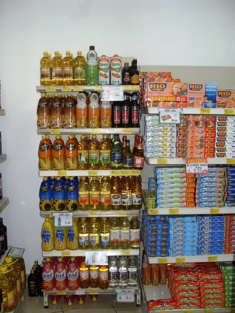 In un piccolo minimarket, gli scaffali sono pieni di bevande in bottiglia di vario tipo e snack confezionati.