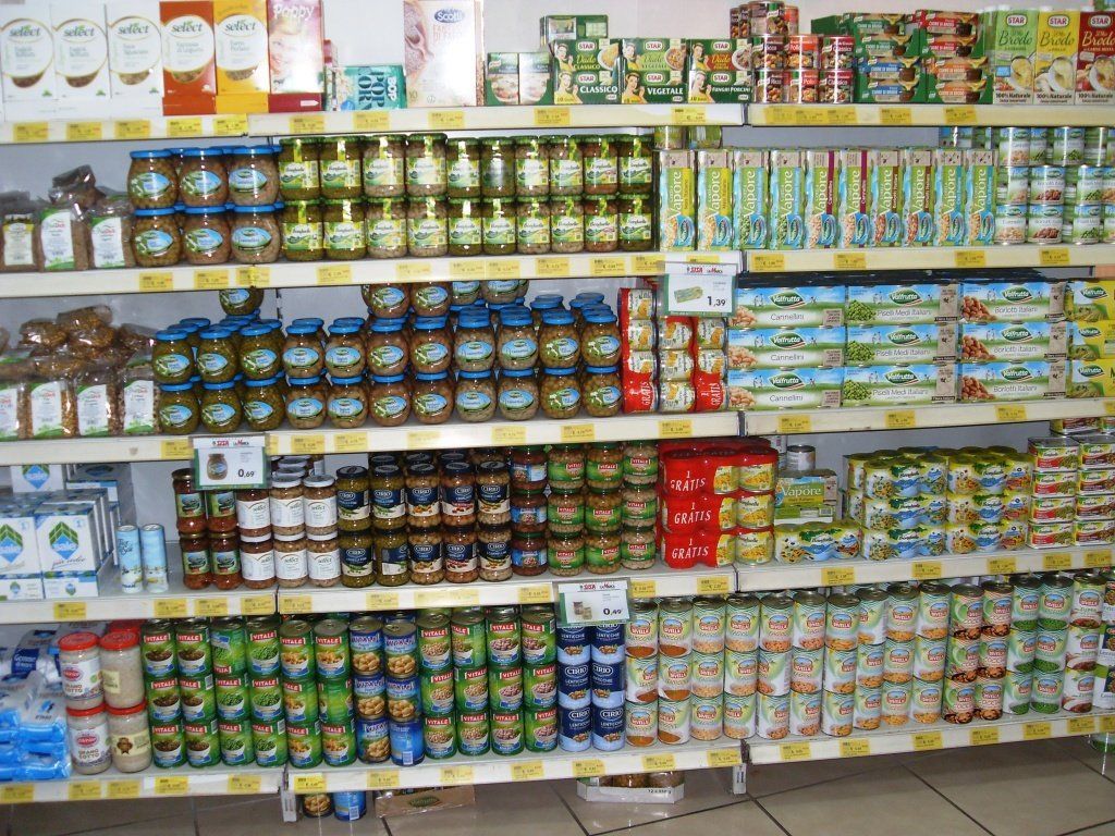 Scaffali pieni di cibi in scatola e in barattolo dai colori vivaci in una corsia di un supermercato.