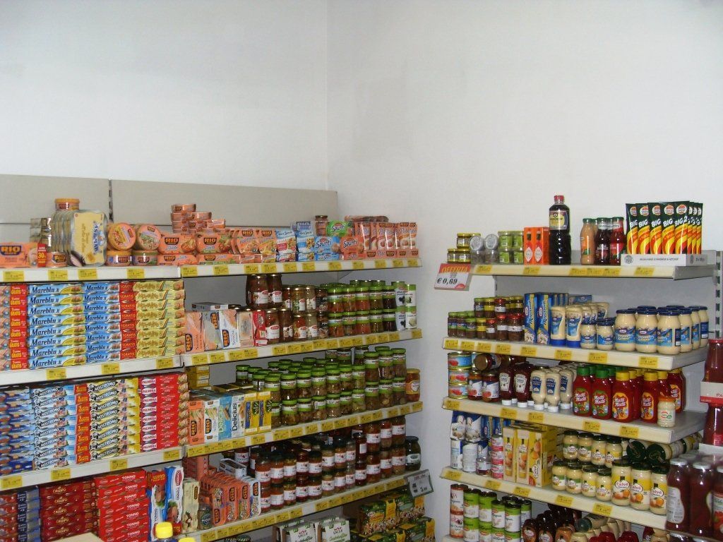 Scaffali del negozio pieni di generi alimentari assortiti in scatola e in scatola in una piccola corsia del mercato.