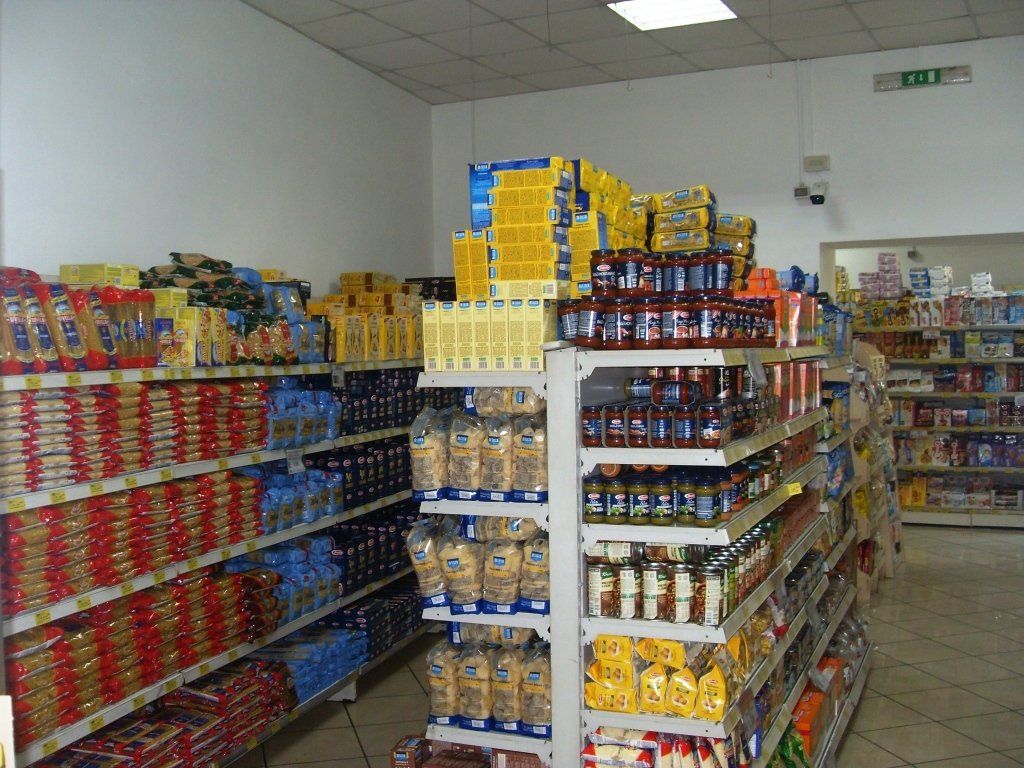 Corridoio di un supermercato con scaffali pieni di conserve, barattoli e alimenti confezionati sotto una luce intensa