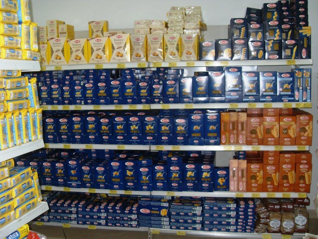 Scaffali di un supermercato pieni di prodotti confezionati di colore blu, giallo e arancione, impilati uno sull'altro.