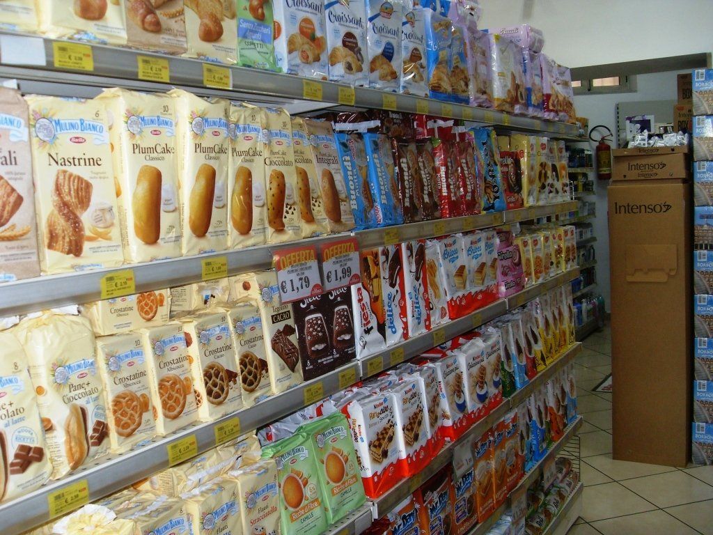 Corridoio di un supermercato con scaffali pieni di snack e scatole di cereali confezionati in modo colorato.