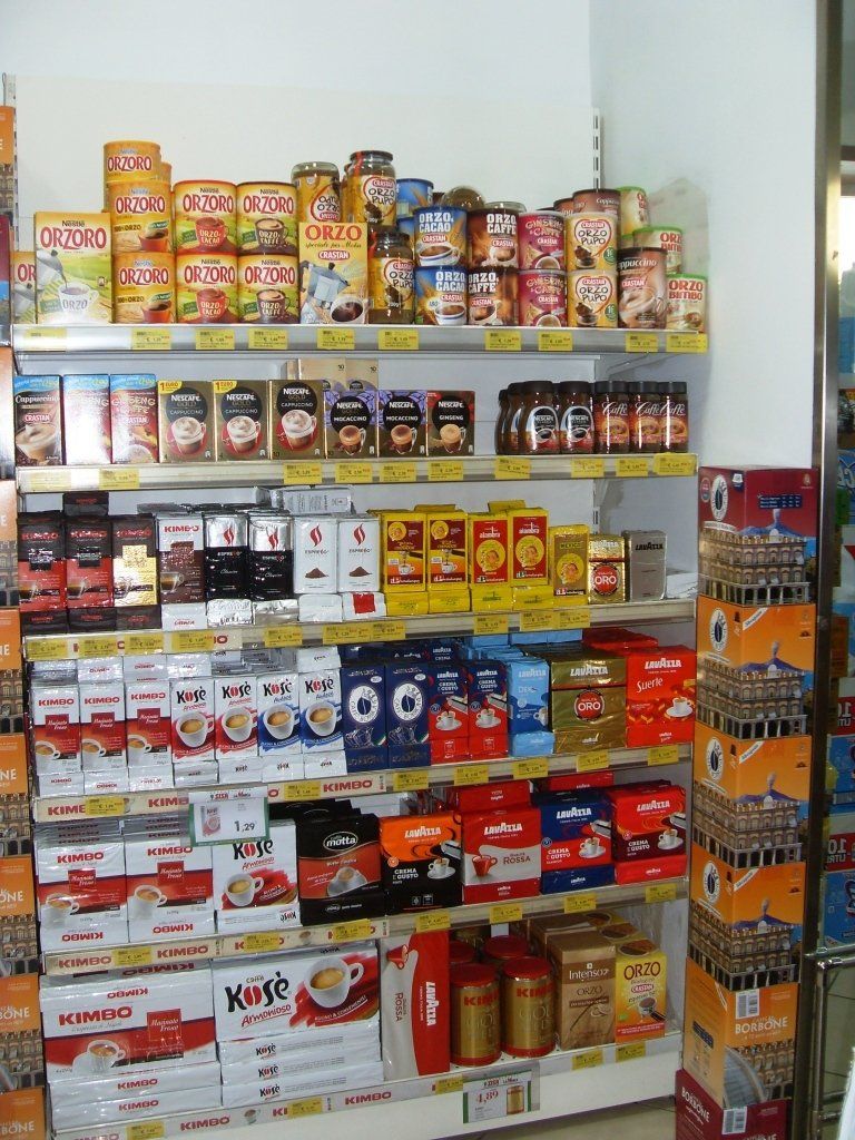 Scaffali pieni di alimenti confezionati e in scatola di vario genere in una piccola corsia del negozio.