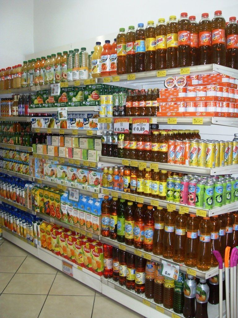 Uno scaffale di un supermercato pieno di bevande in bottiglia, snack e prodotti in scatola di vario genere.