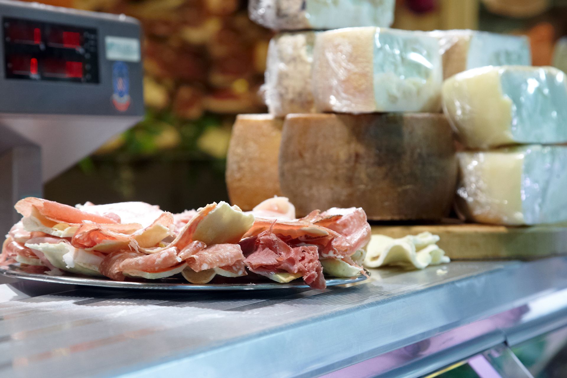 Affettati di salumi sul banco gastronomia accanto a pile di forme di formaggio.