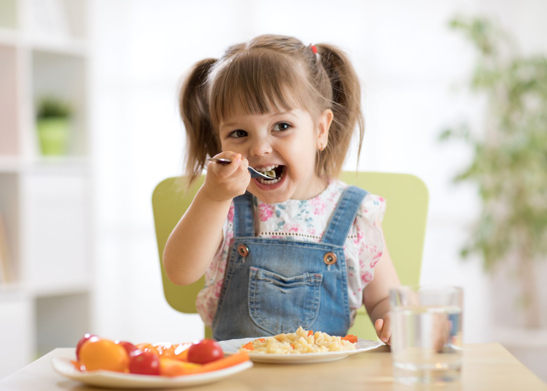 Une petite fille est assise à une table et mange de la nourriture avec une cuillère.