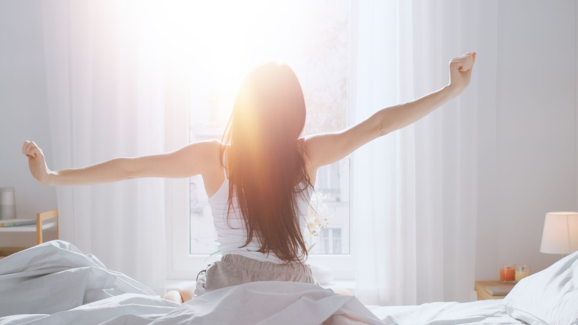 Une femme est assise sur un lit avec les bras tendus.