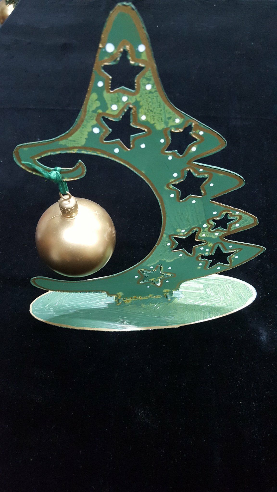 Adorno navideño verde con forma de árbol, con recortes en forma de estrella y una bola colgante dorada.