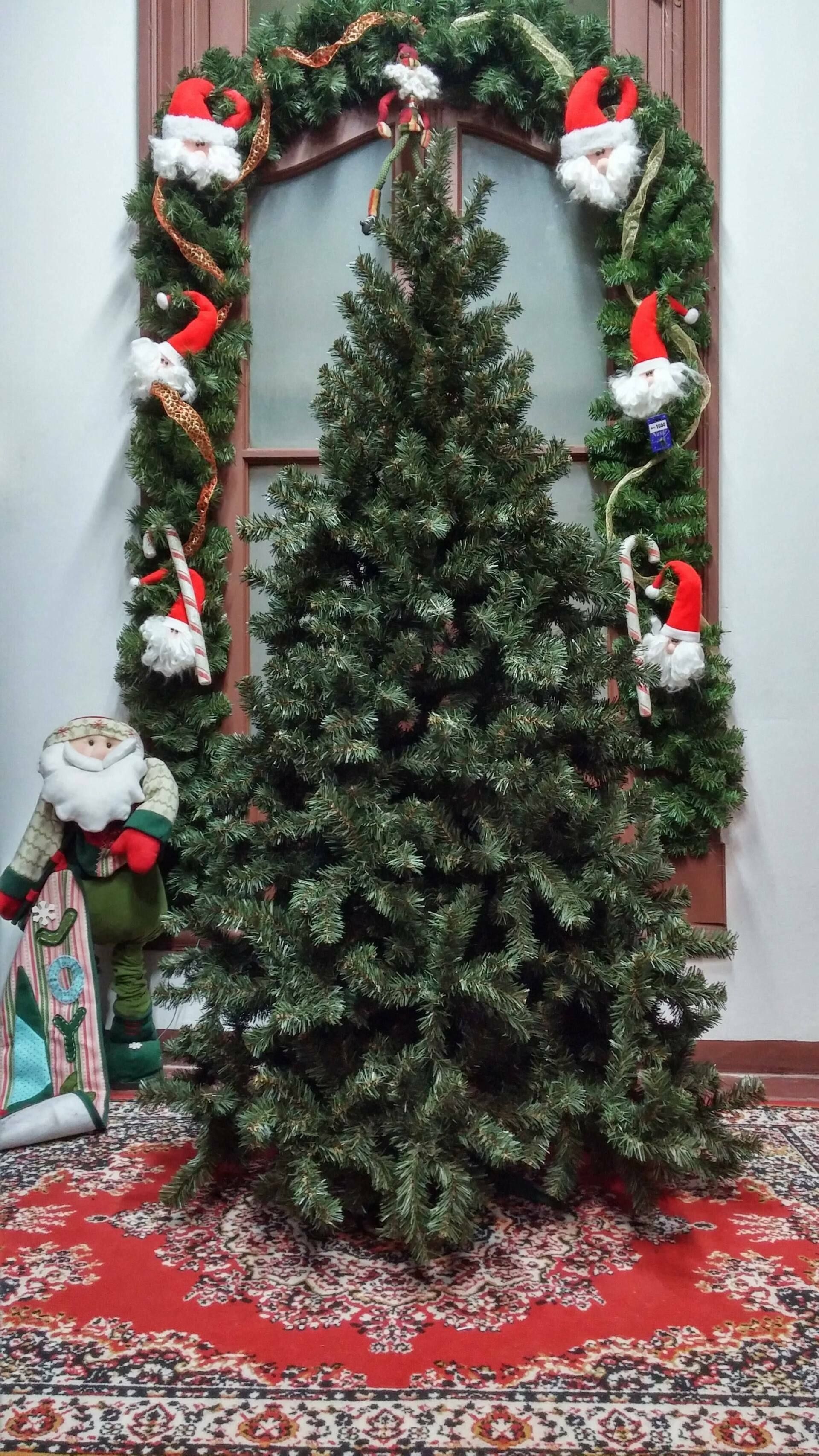 Árbol de Navidad decorado sobre una alfombra roja estampada, enmarcado por un arco de guirnalda festiva con muñecos de nieve