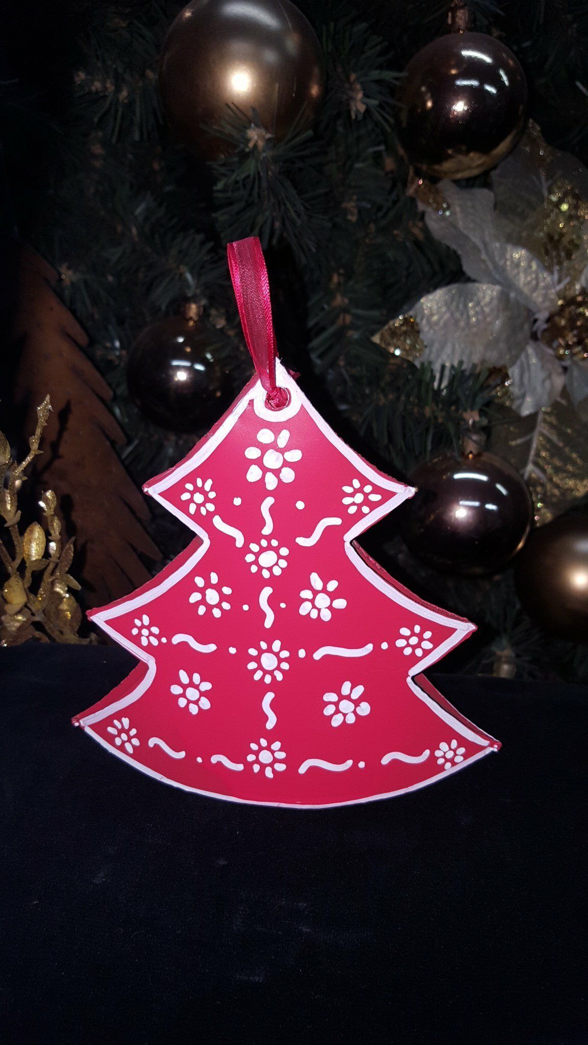 Adorno rosa para árbol de Navidad con motivos florales blancos colgando de un árbol decorado.