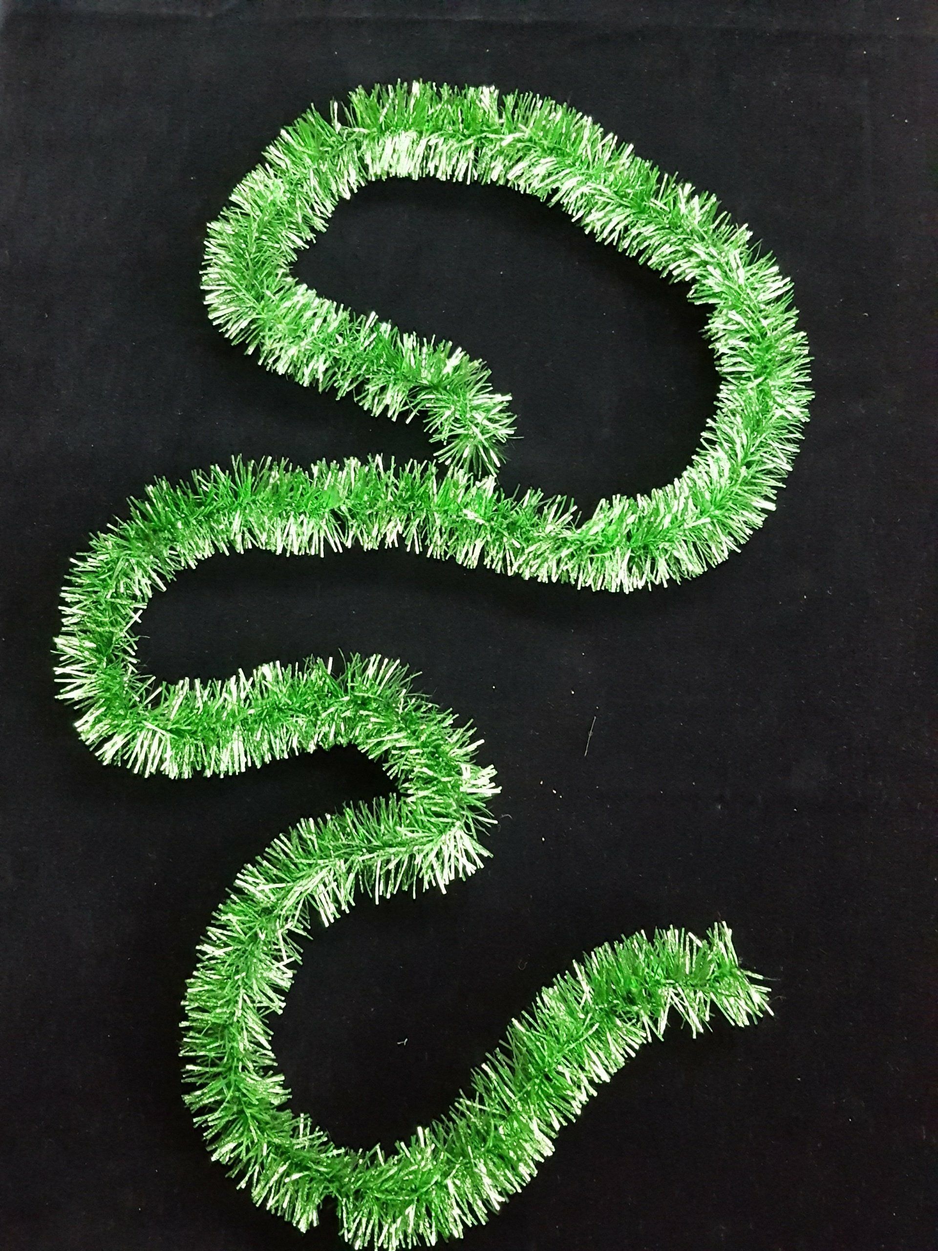 Guirnalda verde y peluda dispuesta en forma de S sinuosa sobre un fondo negro.