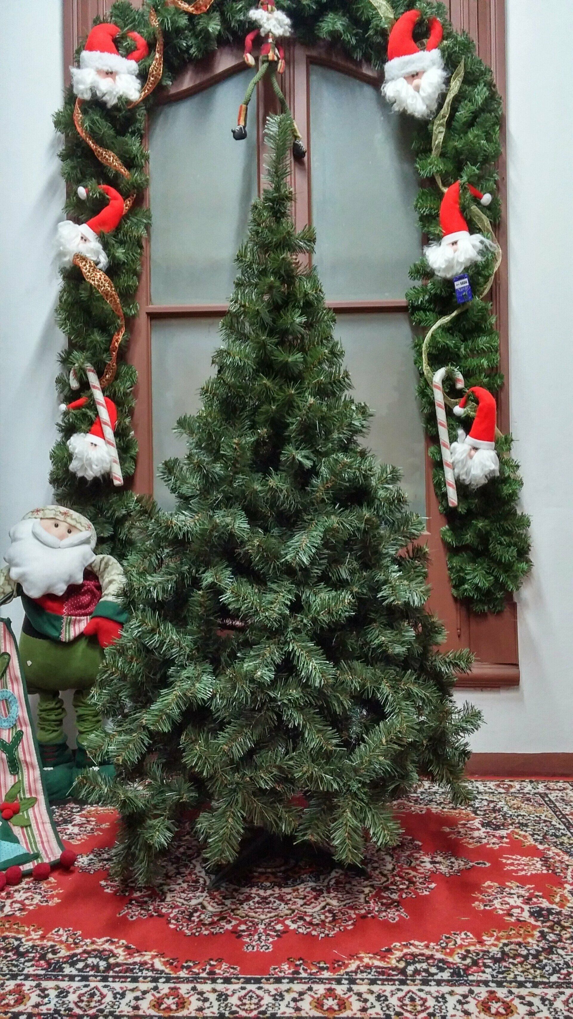Árbol de Navidad decorado frente a una ventana, enmarcado por guirnaldas, figuras de Papá Noel y una alfombra estampada.
