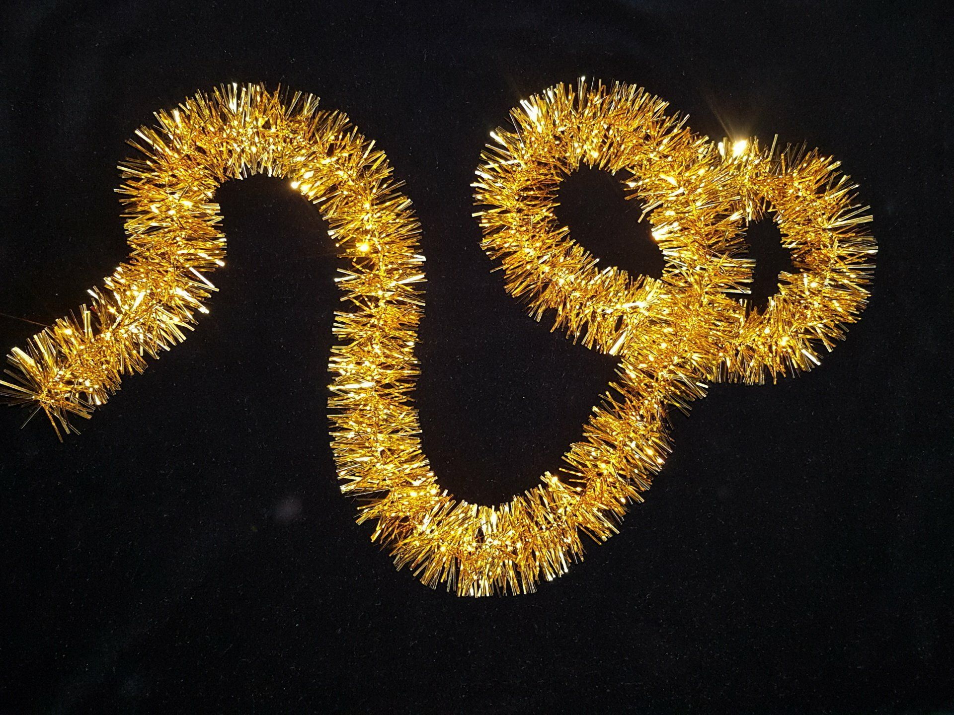 Guirnalda de oropel dorado con forma de línea sinuosa y dos bucles sobre un fondo negro.