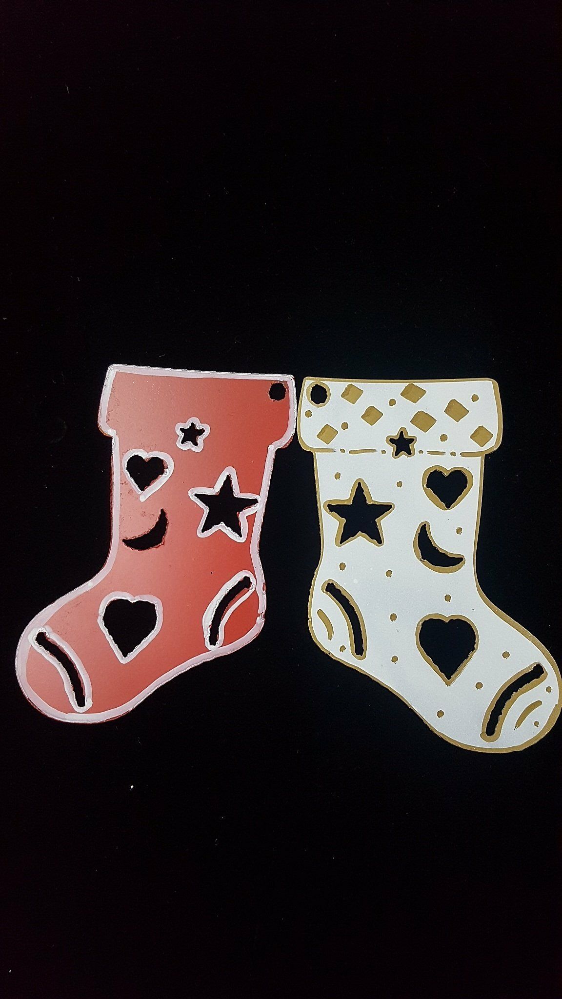 Dos calcetines navideños decorativos, uno rosa y otro blanco, con recortes de estrellas y corazones sobre un fondo negro.