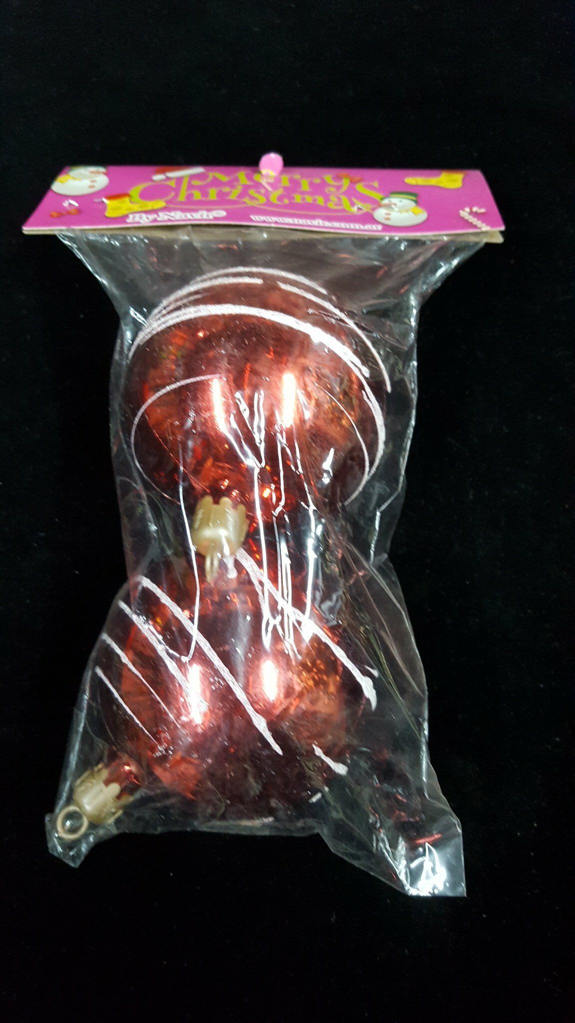 Artículo decorativo rojo en envase de plástico transparente con una tarjeta de cabecera rosa sobre fondo negro.