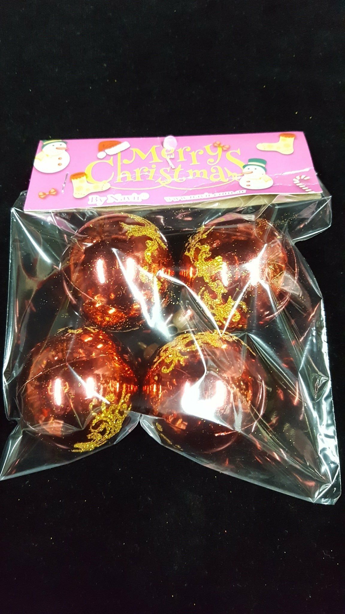 Cuatro huevos de chocolate dorados brillantes en un envase de plástico transparente con una etiqueta rosa sobre fondo negro.