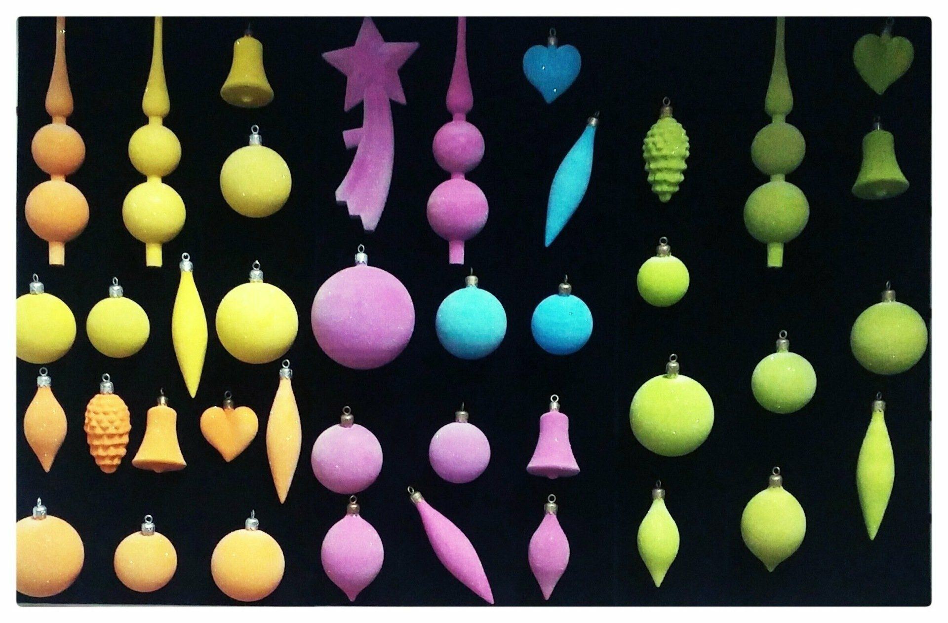 Adornos colgantes coloridos y calabazas en filas sobre un fondo negro.