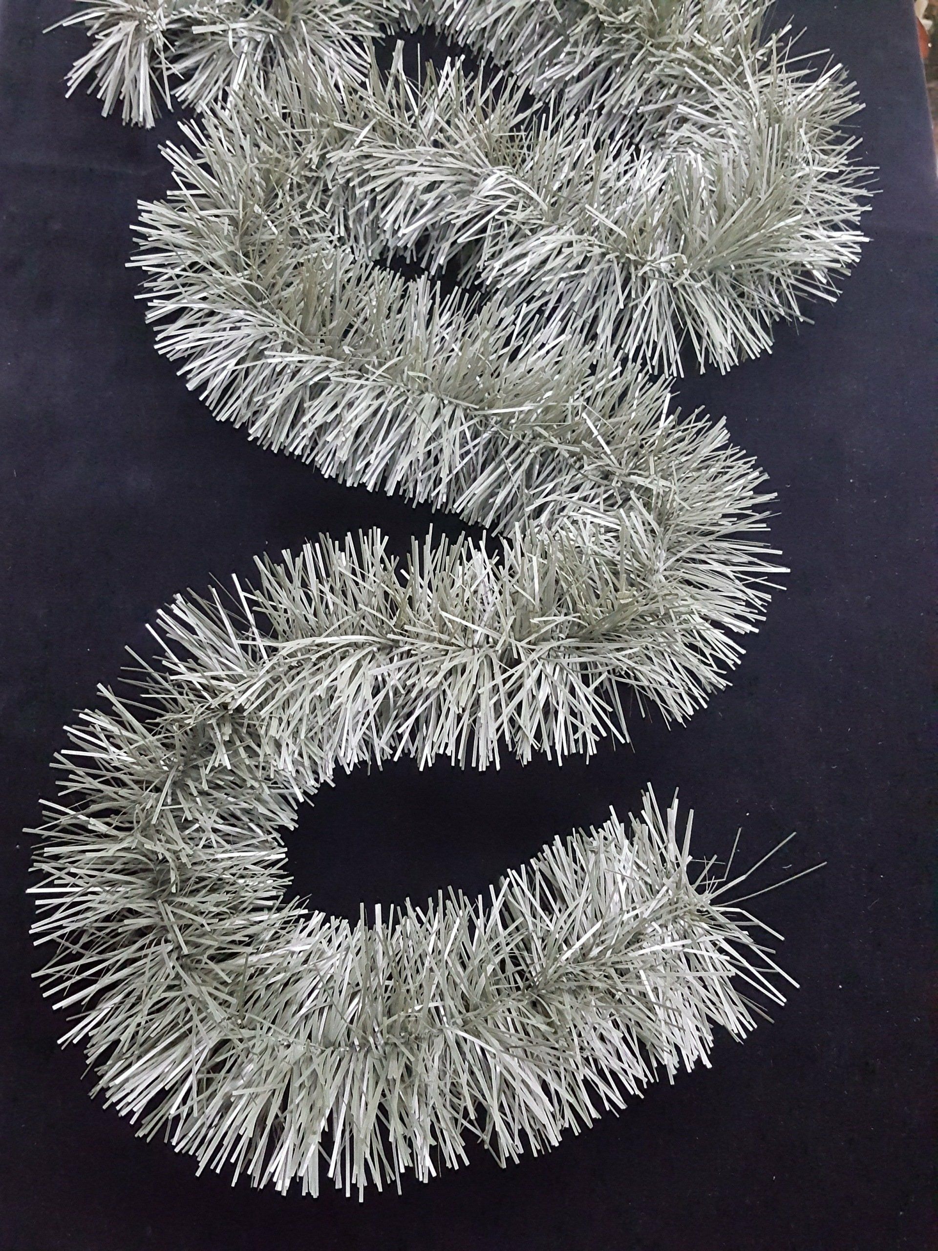 Guirnalda de oropel plateado dispuesta en forma de S ondulada sobre un fondo oscuro.