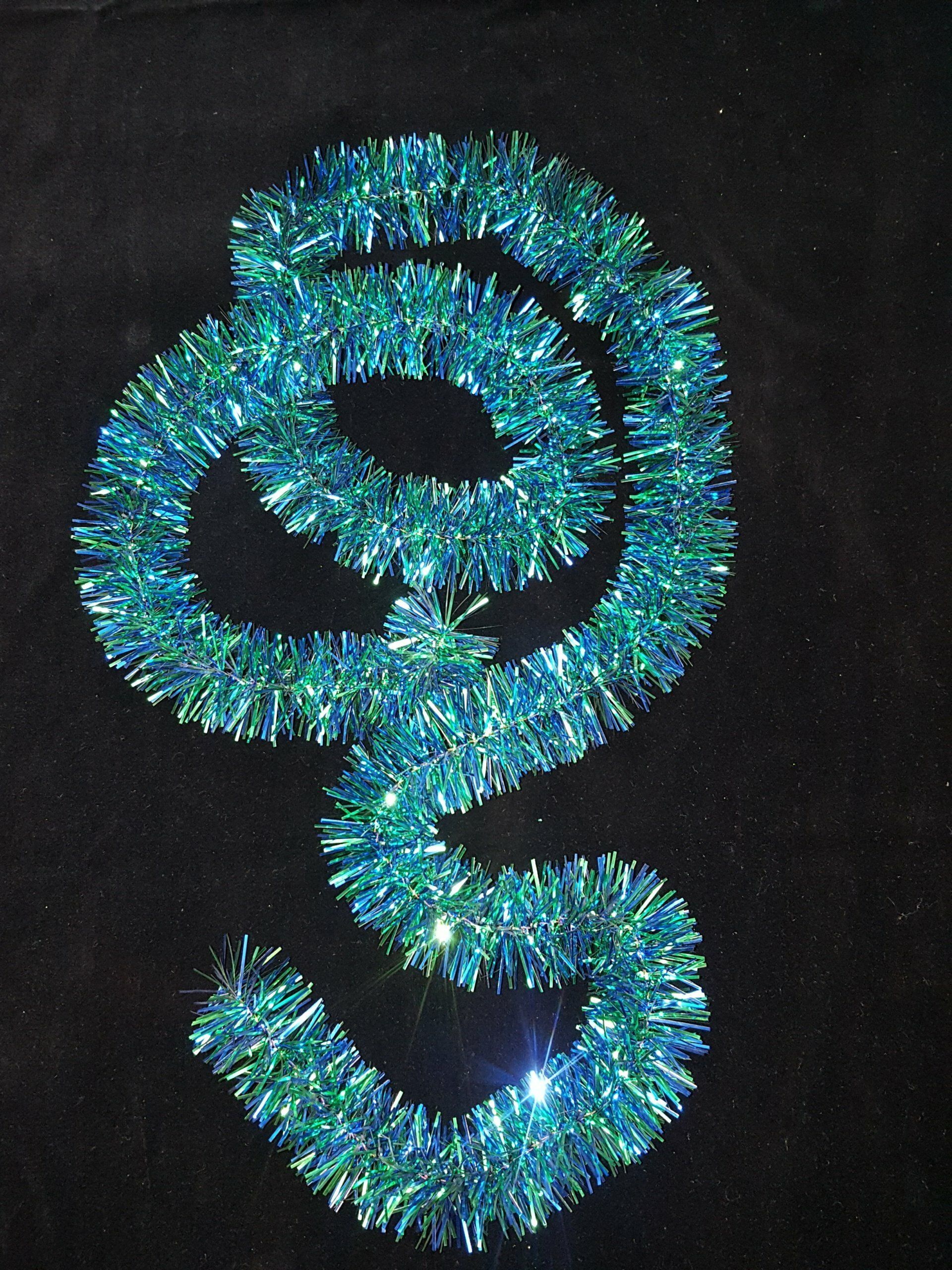 Adorno espiral de oropel azul y verde sobre fondo negro.