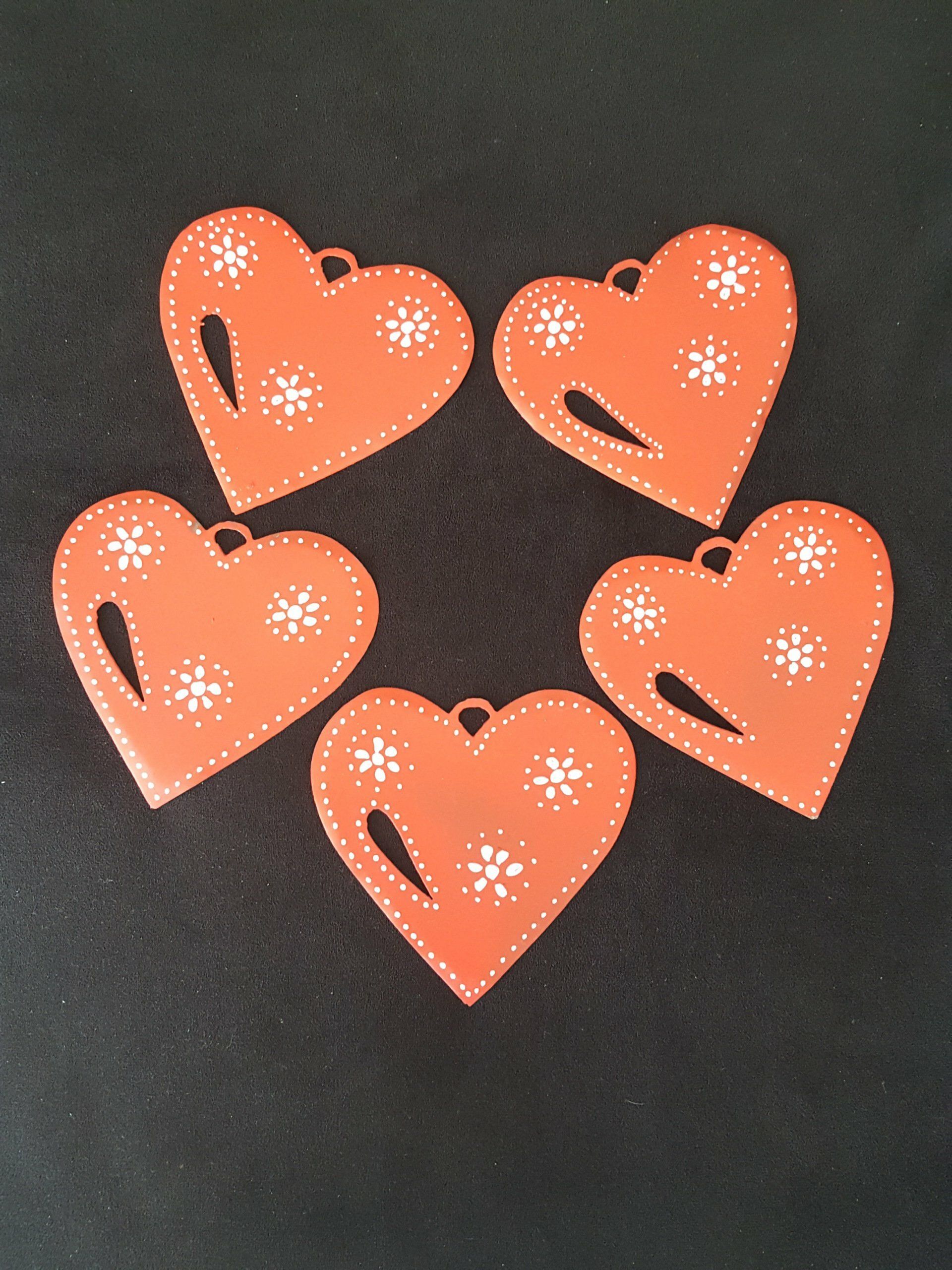 Cinco recortes de papel naranjas con forma de corazón y motivos florales blancos sobre un fondo oscuro.