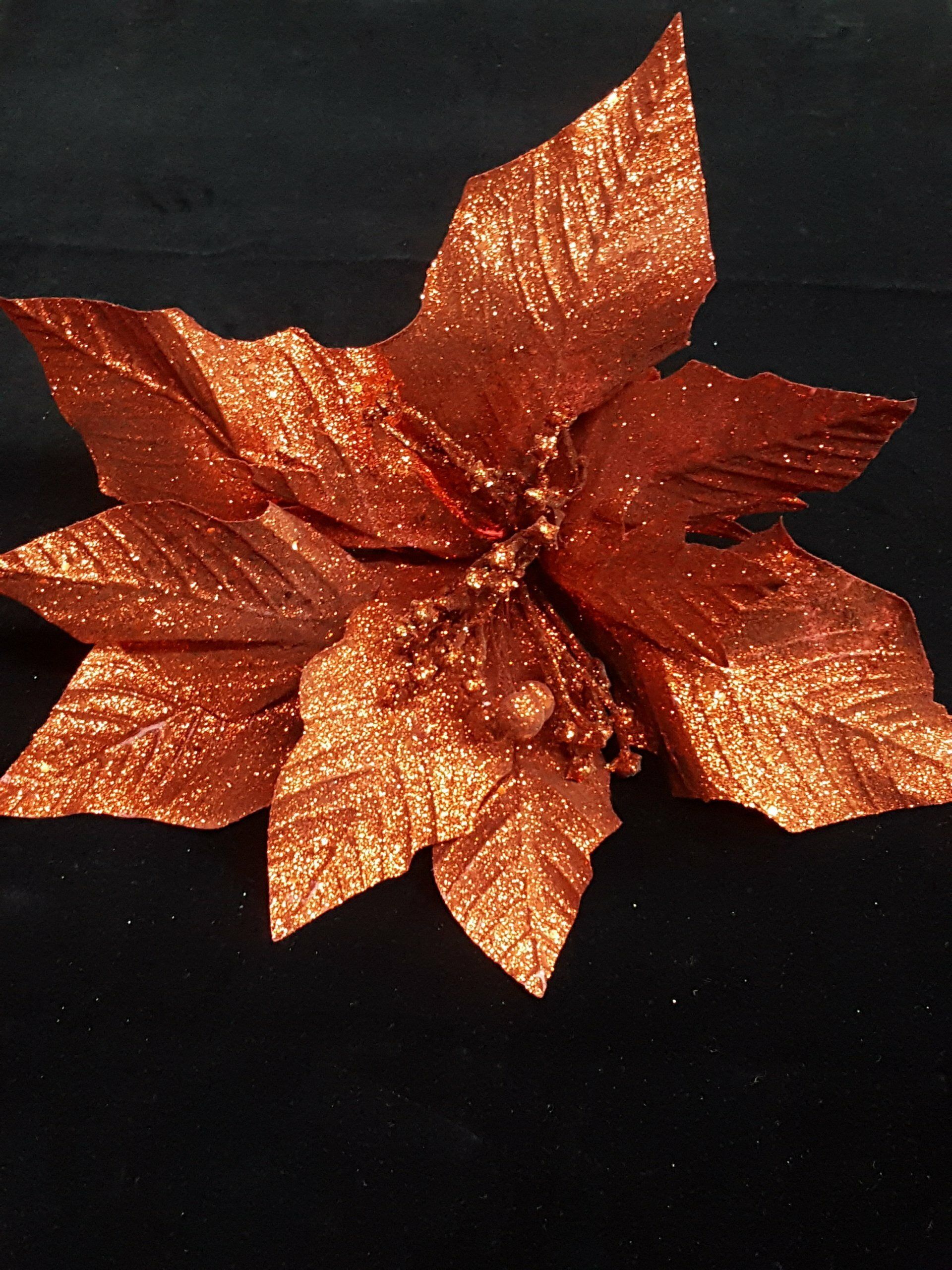 Decoración de flor de Pascua color cobre con hojas brillantes sobre fondo negro.