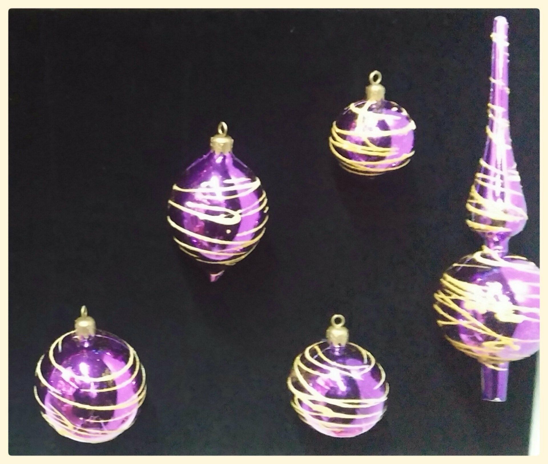 Adornos navideños a rayas moradas y doradas sobre un fondo negro.