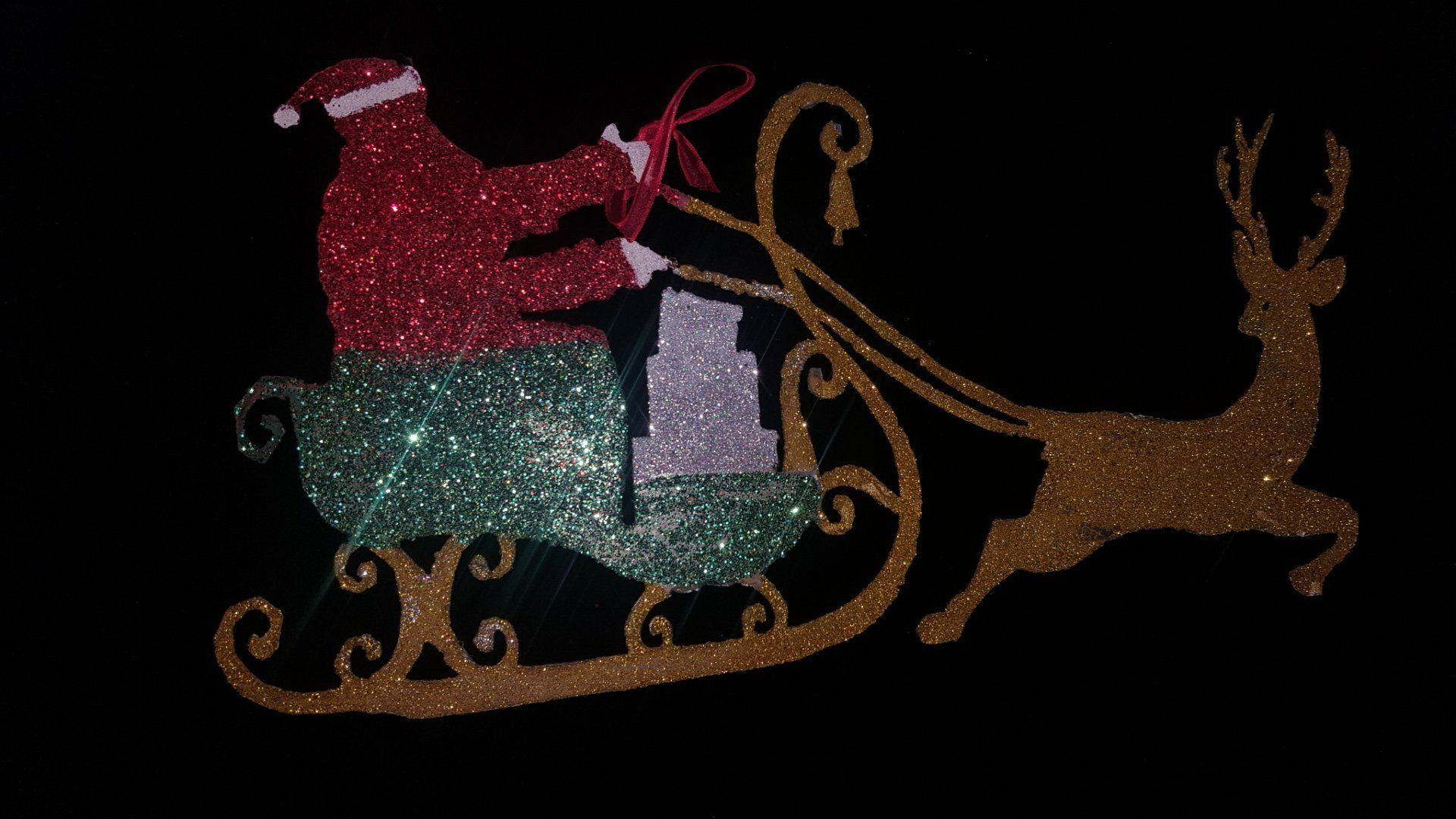 Papá Noel en un trineo rojo tirado por un reno, brillando con luces rojas, turquesas y doradas sobre un fondo oscuro.