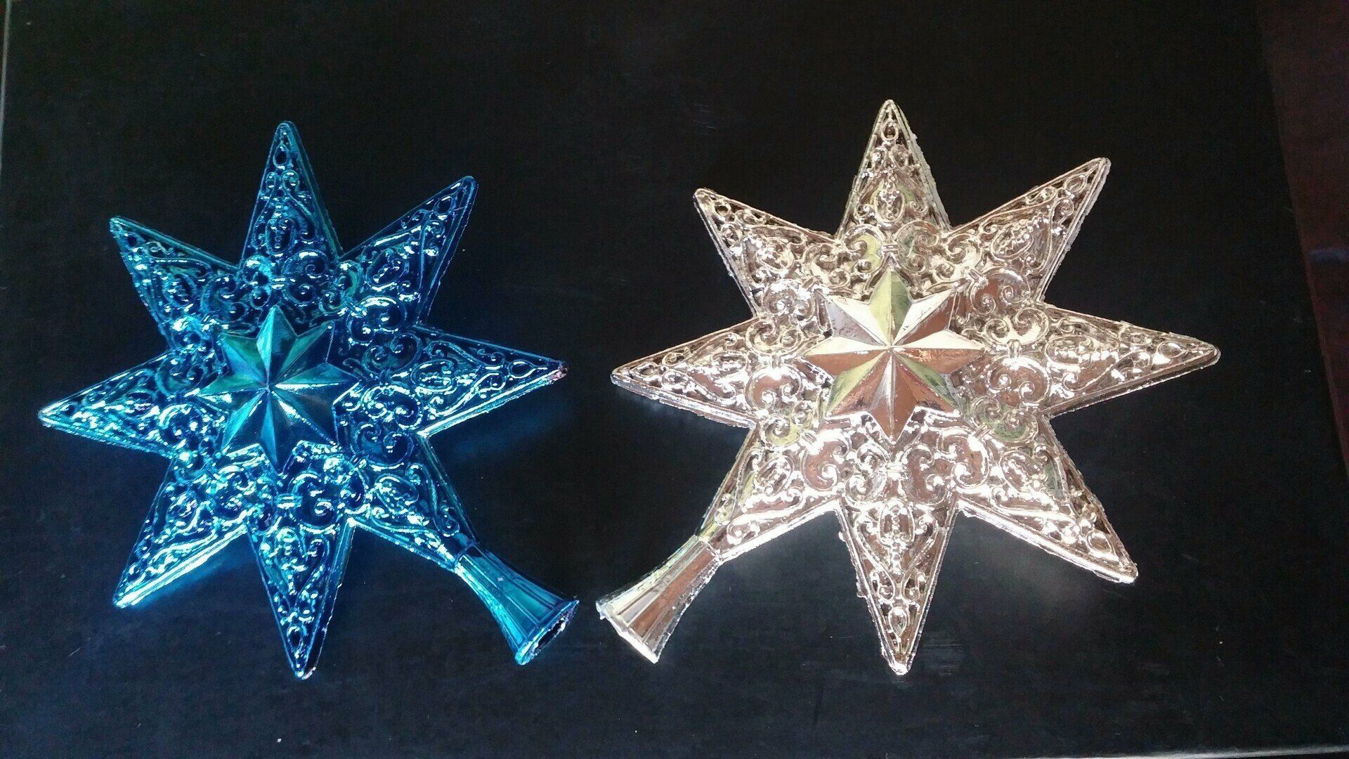 Dos adornos brillantes en forma de estrella, uno azul y otro plateado, sobre un fondo oscuro.
