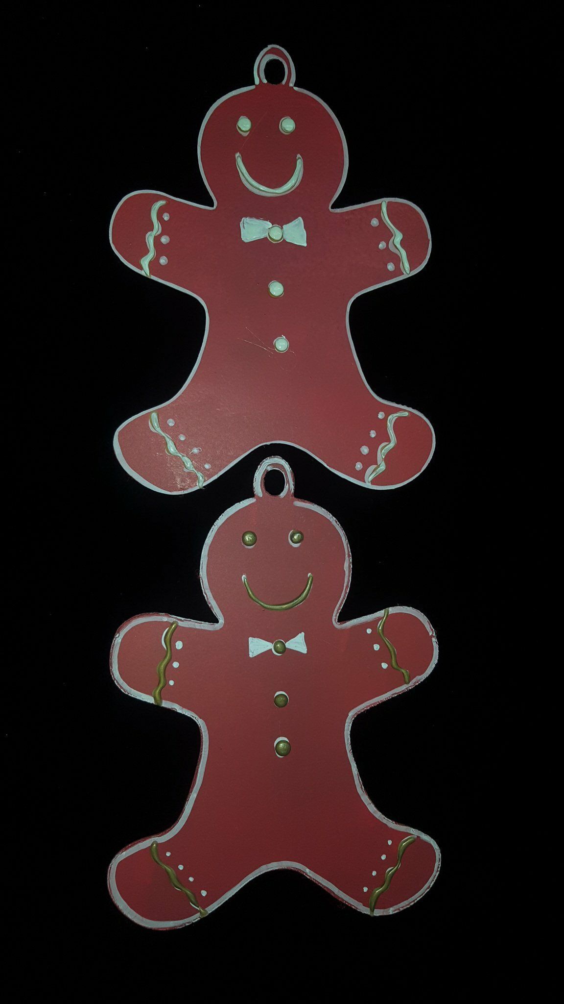 Dos figuras de pan de jengibre rojas, una encima de la otra, sobre un fondo negro.