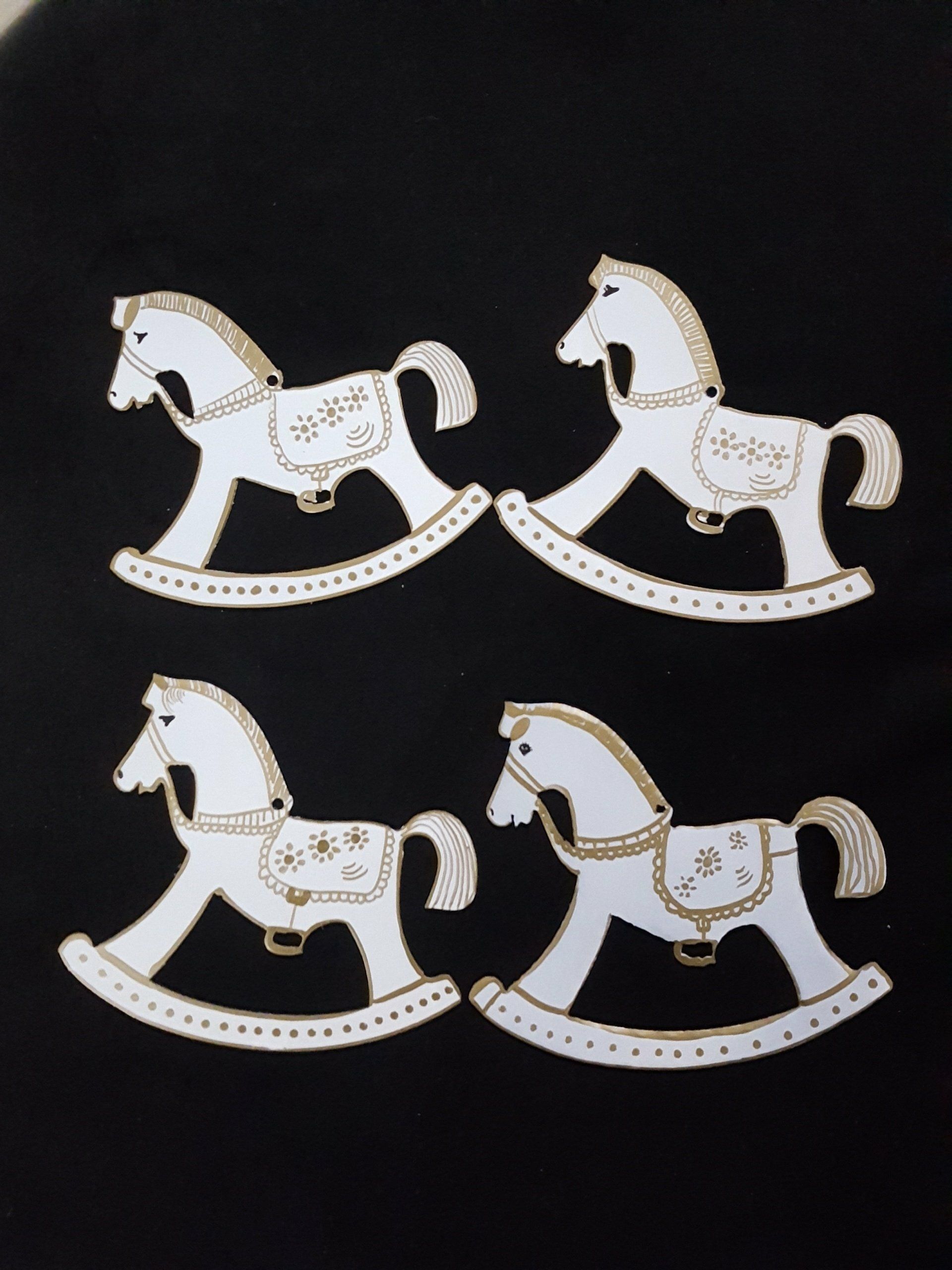 Cuatro adornos de caballitos mecedores blancos con detalles dorados sobre un fondo negro.