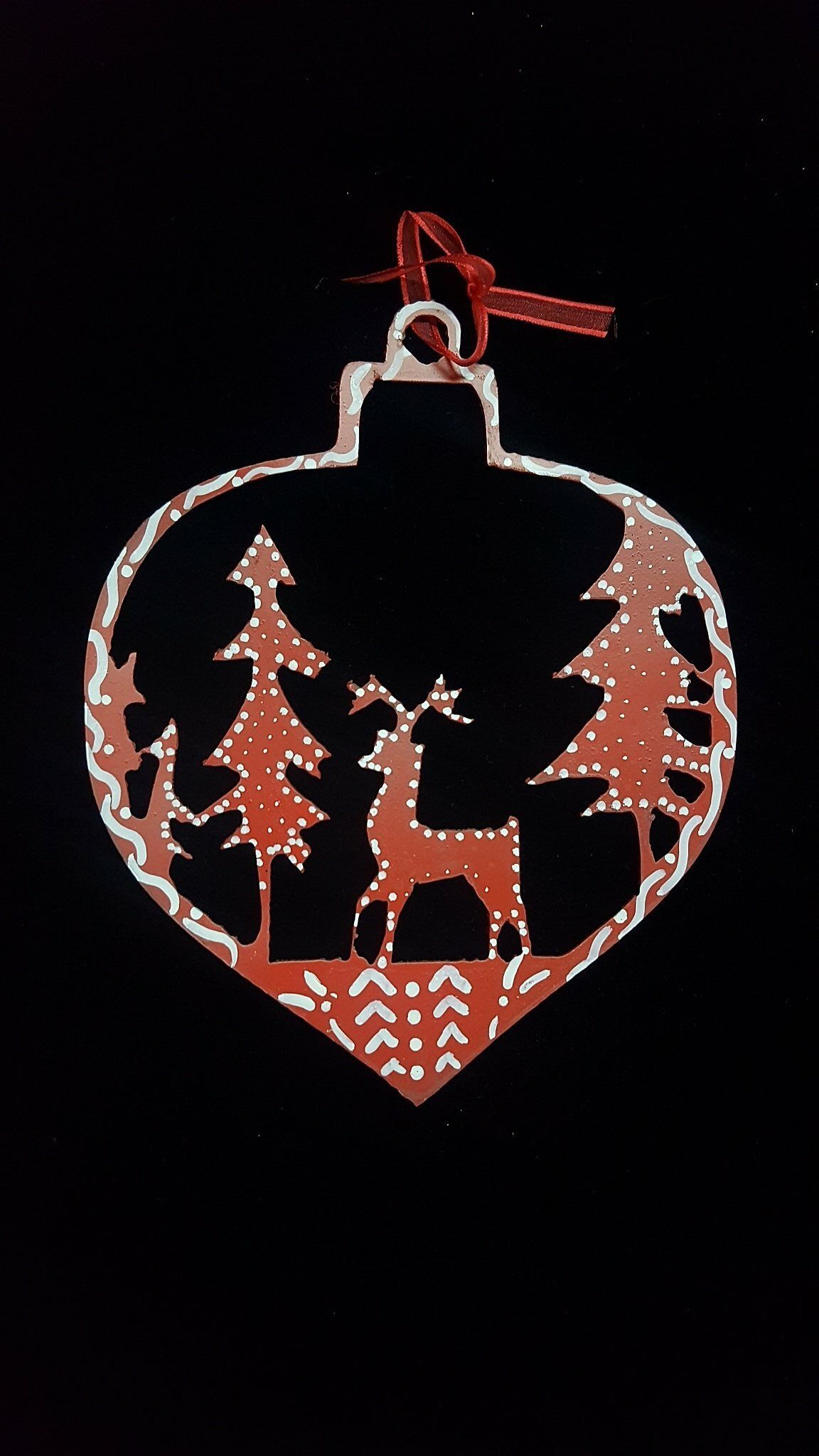 Adorno rojo en forma de corazón con ciervos y pinos, delineados en blanco y naranja sobre un fondo negro.