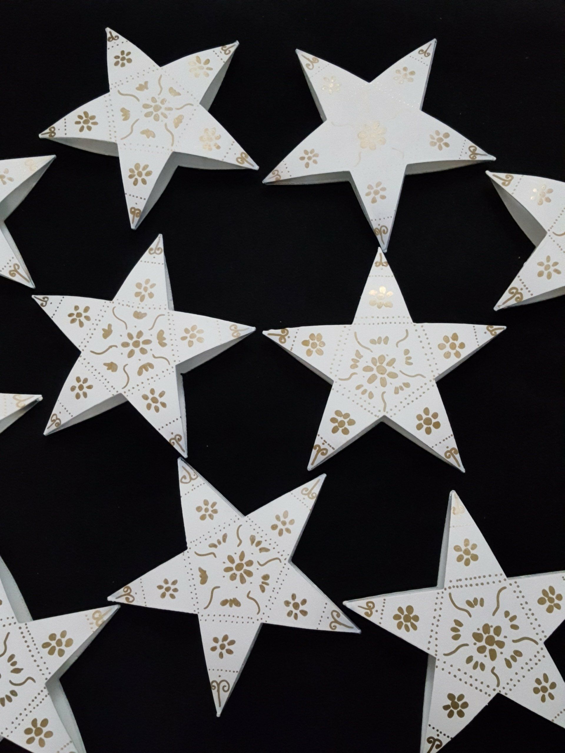 Adornos de estrellas de papel blanco con motivos dorados esparcidos sobre un fondo negro.