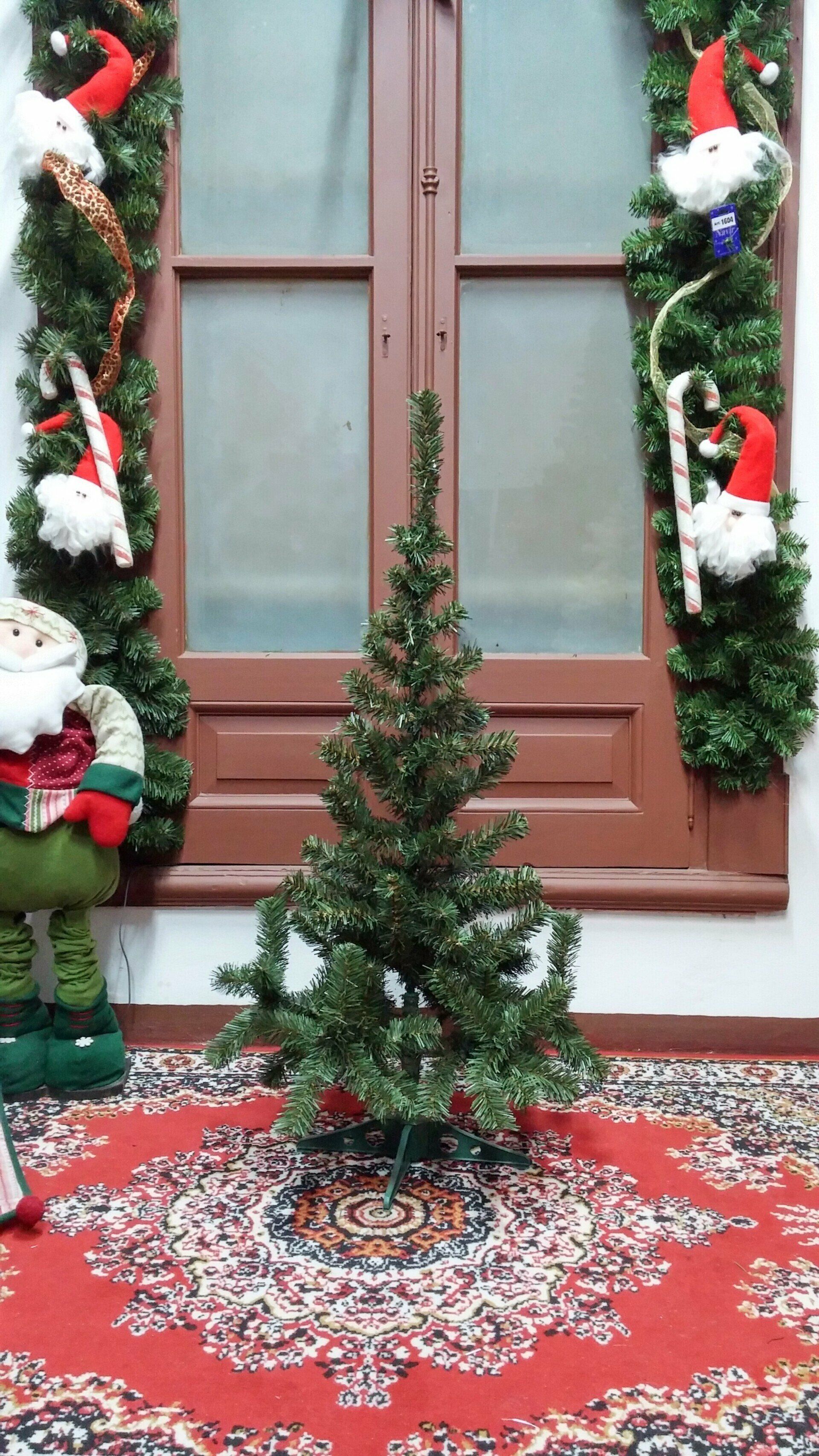 Pequeño árbol de Navidad decorado sobre una alfombra roja estampada frente a una ventana con guirnaldas