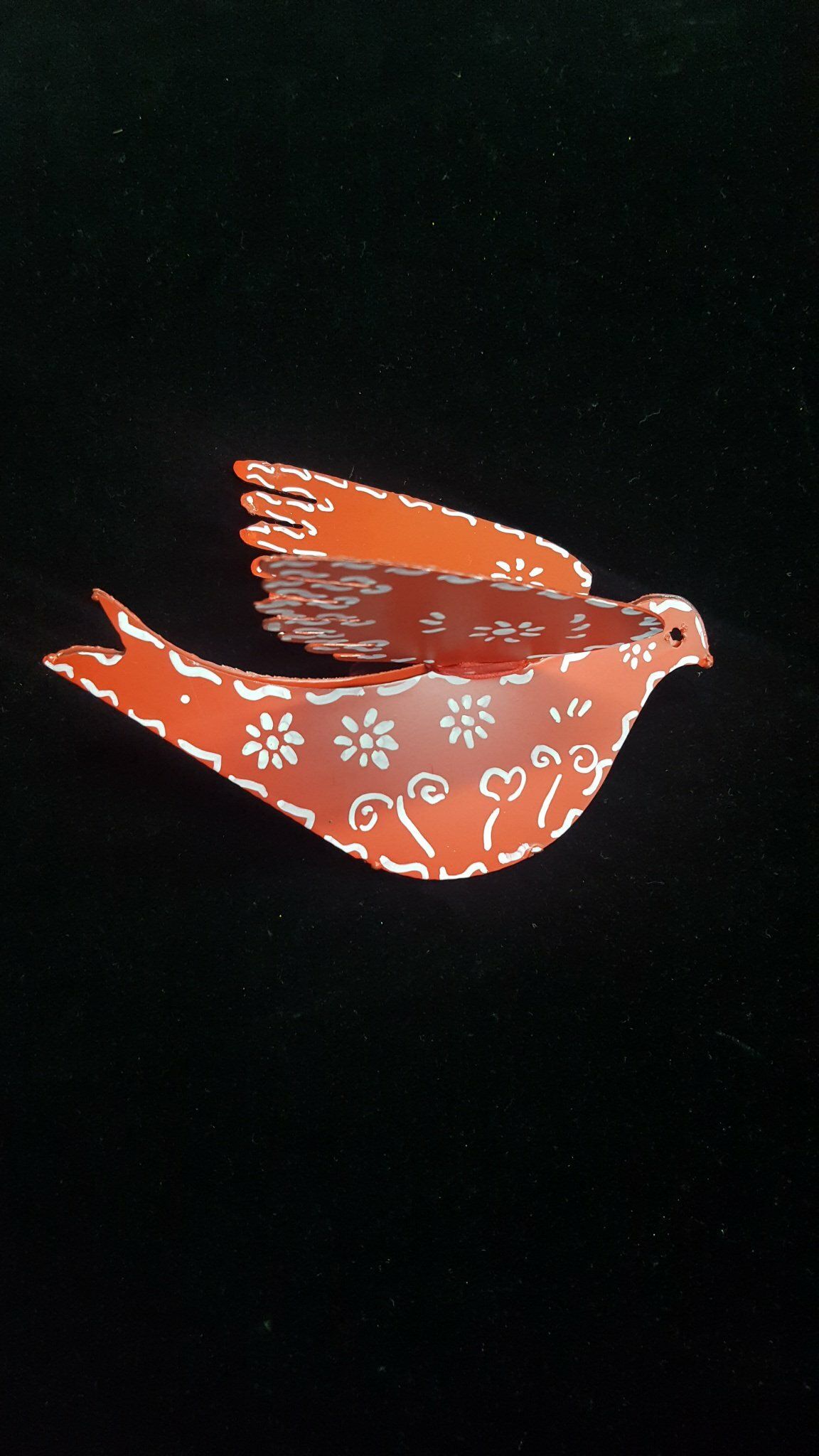 Pájaro naranja con estampados florales blancos volando sobre un fondo negro.